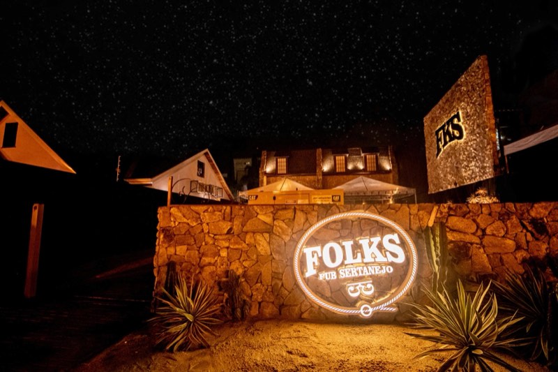 Entrada do Folks Pub à noite, com o letreiro aceso